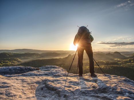 Artist set camera and tripod to photograph the sunrise on a rocky summit. Artist works in nature