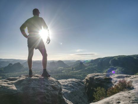Man doing stretching exercise outdoors.  Extreme runner climbs the mountain top and see wide valley