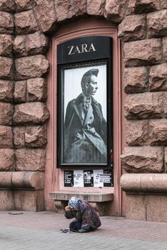 Kyiv, Ukraine - Nov 16, 2019: Disadvantaged and impoverished people on the street of Kiev. Beggar homeless woman asks for alms in front of a fashion store advertising