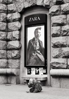 Kyiv, Ukraine - Nov 16, 2019: Disadvantaged and impoverished people on the street of Kiev. Beggar homeless woman asks for alms in front of a fashion store advertising. Black and white image