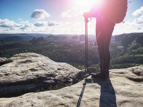 Tourist boy with backpack and sticks in foggy mountain range standing on rocky top on bright blue morning sky background.