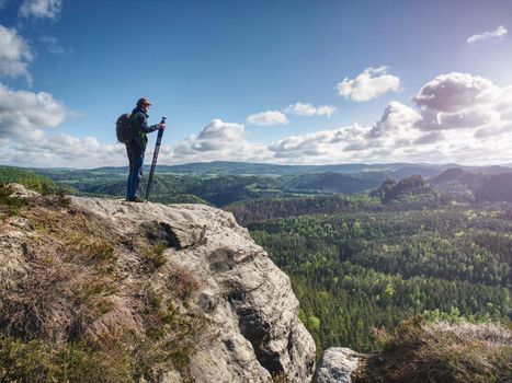 Wild nature photographer or traveler with tripod standing on stony hill above valley in nature park.