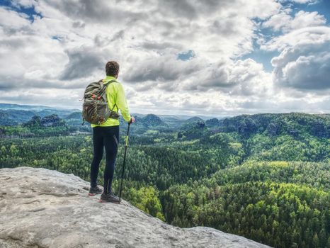 Man trail runner stop on mountain top for relax. Trail athlete in light green lerzey and black leggings on the trail with long deep valley on the background