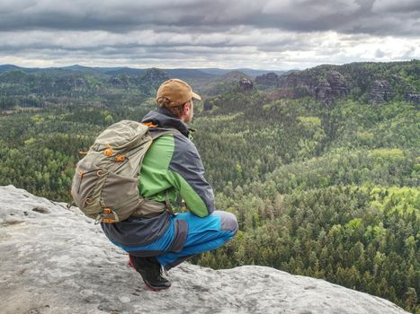 The body of man with a backpack and running shoes stands on top of a rock against the background rocky valley high in the mountains. The concept of tourism 