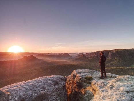 Man walking over rocky summit at rising Sun. Beautiful moment the miracle of nature. Vintage effect.