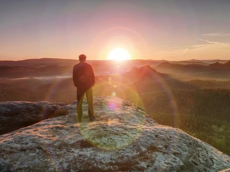 Man hiker at mountain peak. Marvelous daybreak in misty landscape. 