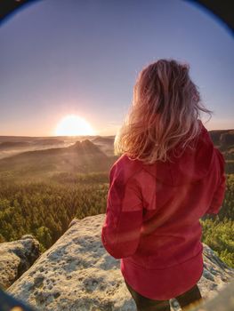 Blond hair girl tourist enjoy successful achievement of rocky summit with fantastic view into morning hilly landscape.