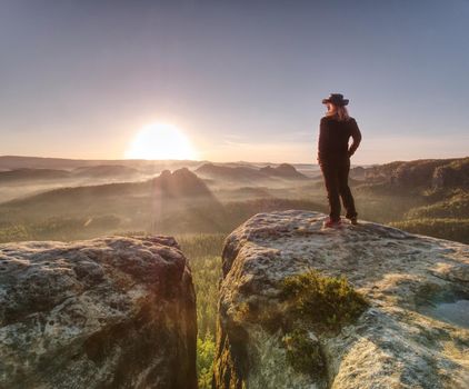 Beautiful long blond hair woman wearing cowgirl hat and dark trekking clothes  while resting in sunlit on summit.