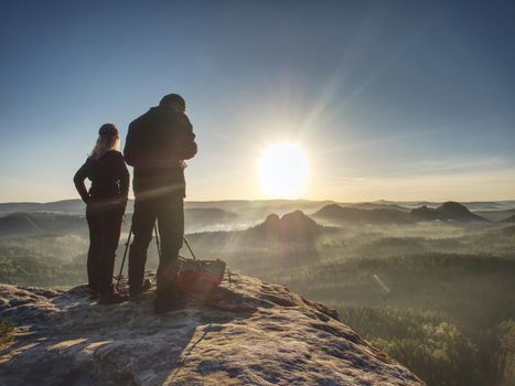 Photographer check viewfinder of camera on tripod and framing natural scene. Lady and man create art on cliff and takes photos