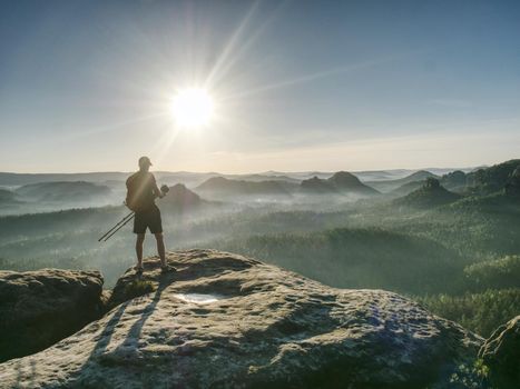 Artist photographer stay as model on rock with sunset in background. Photographer works. 