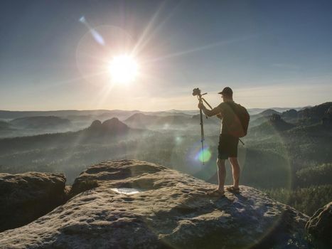 Man photographer taking photo on sunset mountain peak. Hiker in shorts and backpack on sweaty bag