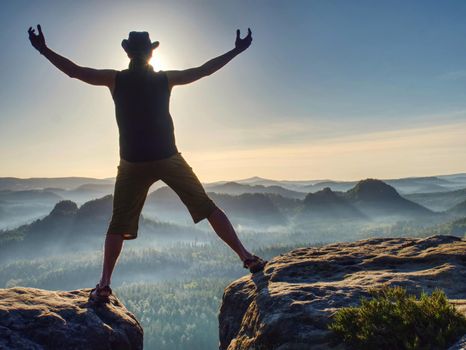 Summit achievemnt. Hiker in black celebrate triumph between two rocky peaks. Wonderful daybreak in rocky mountains