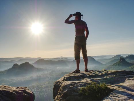 Cowboy style hiker man on cliff of park is watching over misty morning valley to Sun. Man body with akimbo arms