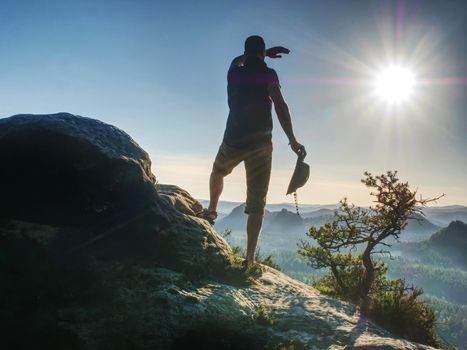 Hiker girl with leather cap stay with hands in pocket on cliff edge above misty valley. Marvelous autumn morning in pure nature