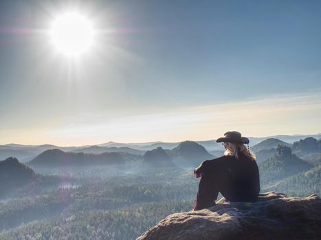 Attractive woman wearing a straw cowboy hat is sit in front of large valley, looking out across the horizon.