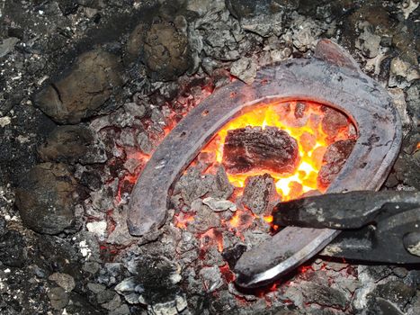 Blacksmith working metal stove, horse shoe preheating for adjustment on anvil. Blazing furnace at the blacksmith working place