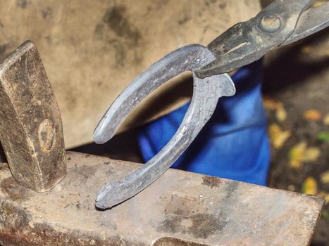 Detail to blacksmith arms forge horseshoe with hammer on anvil. Ancient craft. Village craft. Blacksmith working metallurgy
