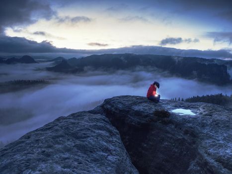 Woman in hands hold the sun. Hiker girl sit in dark night above clouds and wait for sunrise. Summit on top of the mountain delighted with the magnificent first sun  rays.