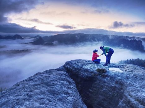 Night photo A woman shows magical lightning lantern to her man.  Woman sits on a rock and shines to misty darkness.  First Sun rays appear in the clouds