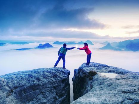 Hikers or climbers in mountains. Couple hold the light  high above danger gulch between rocks. Night photo in misty mountains. Lovers standing on rocky mountain peak