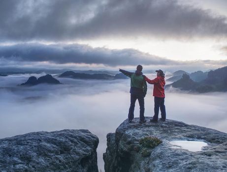 Lovers mirroring in water eye at mountain summit above thick mist.  Climbing couple at top of summit with amazing aerial view