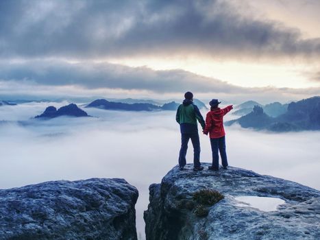 Lovers mirroring in water eye at mountain summit above thick mist.  Climbing couple at top of summit with amazing aerial view