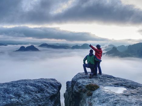 Lovely heterosexual Couple looking at far sunrise in heavy clouds. The dark night in foggy mountains ends.