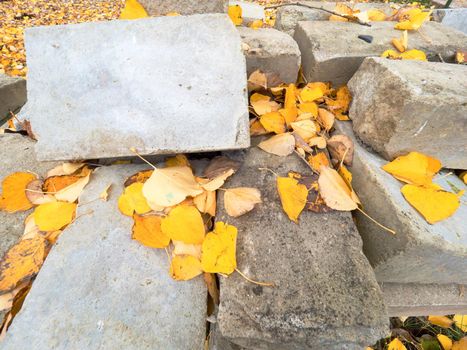 Pile of natural stones and concrete blocks cubes for making outdoor pavement tiles. Chaotic stack of broken tiles with cover of yellow poplar leaves