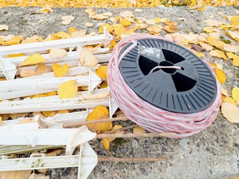 White HDPE pole with insulator hooks wor electric wire built fence for cattle protection surrounded with dry grass and flowers on warm summer day