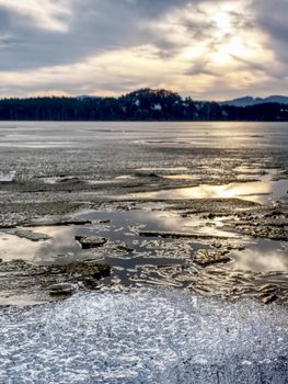 Exposed shore under melting ice. Close up view to border between ice and dark water.  Warm summer on north.