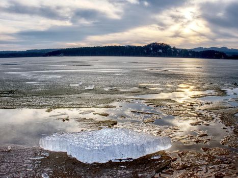 Exposed shore under melting ice. Close up view to border between ice and dark water.  Warm summer on north.