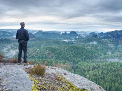 Man stop for watching misty landscape. Moment on the edge of a cliff high above the misty forest landscape