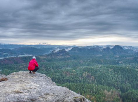 Man stop for watching misty landscape. Moment on the edge of a cliff high above the misty forest landscape