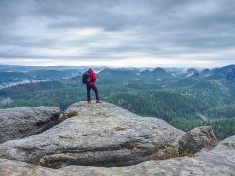 Outdoor photographer with tripod and camera on rock thinking. Mist in valley bellow. 