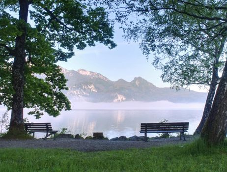 Empty bench at the lake beach. Magnificent lake in South Bavaria, Germany.  The concept of walking and eco-tourism. Water reflects the surrounding mountains and forest