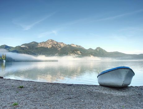 Modern sport fishing paddle boat anchored on shore of the lake bay. Peaceful level of lake. Windless sunny day.