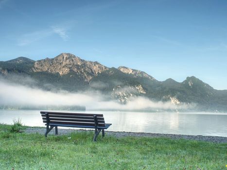 Bench under a tree on a lake shore. Mountains at background. Take a rest near blue green lake.  Beautiful mystical lake.