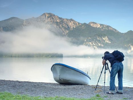Photo traveler is taking memory photo of lake scenery. Blue lake between high mountains, peaks touch in blue sky. Travel lifestyle concept