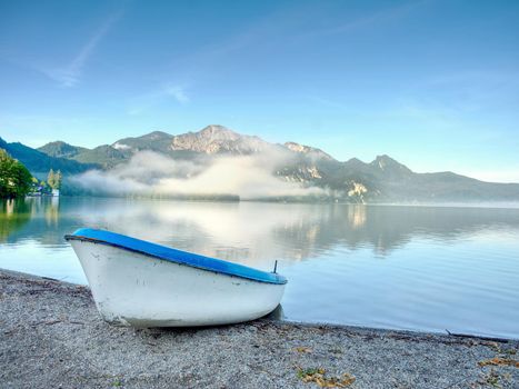 Fishing boat on shore on background of picturesque landscape of lake and green nature around in bright sunny summer day.