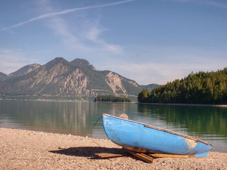 Boat on the stony shore of a mountain lake Walchensee. Warm  spring morning with reflection of mountains in green water level.