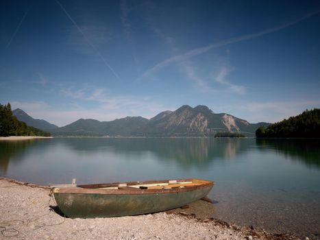 Abandoned fishing boat on bank of Alps lake. Morning lake glowing by sunlight.
