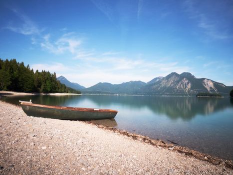 Fishing boat on shore on background of picturesque landscape of lake and green nature around in bright sunny summer day.