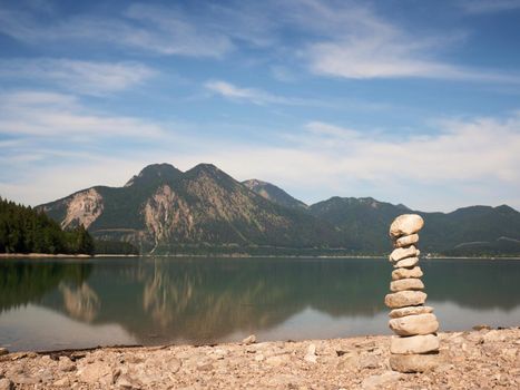 Balanced stone pyramide on shore of blue water of mountain lake. Blue mountains in water level mirror.