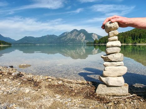 Pyramid of flat stones on a pebbly lake beach, the mountains mirroring in smooth water level.