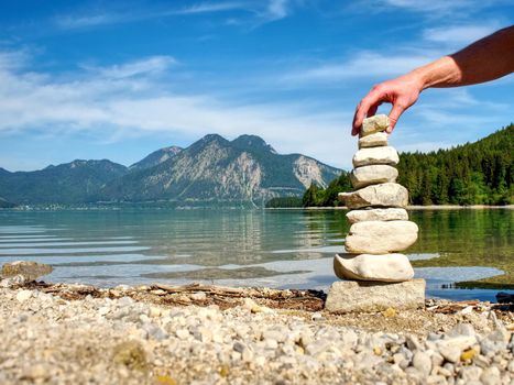 Balanced stone pyramide on shore of blue water of mountain lake. Blue mountains in water level mirror.