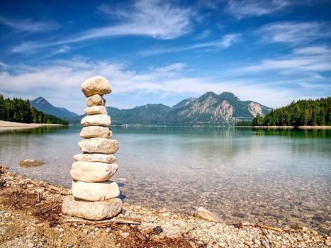 Building of stone pyramide on shore of blue water of mountain lake. Blue mountains in water level mirror