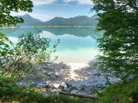 Pebble or rocky shore of the mountain lake, in the distance you can see the sharp Alps mountains