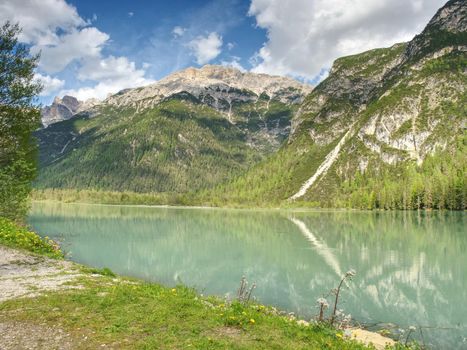 Pebble or rocky shore of the mountain lake, in the distance you can see the sharp Alps mountains