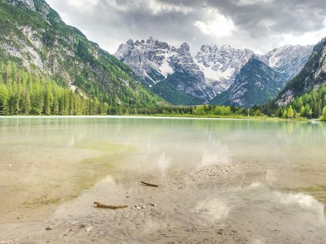 Blue green lake between sharp rocky mountains.  Smooth water surface, the peaks are illuminated by the sun's rays, the Alps.