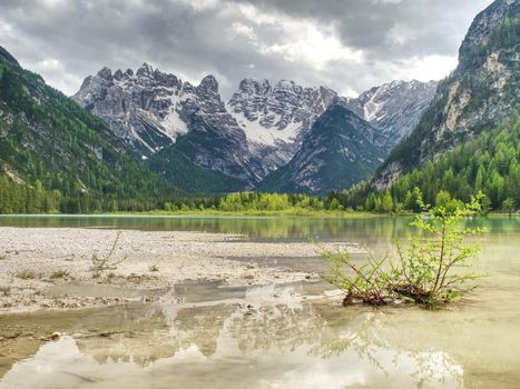 Lovely nature scenery with rocky peaks above coniferous forest and beautiful lake. Smooth surface of water reflects mountains